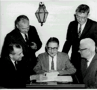 group around desk watching McKenna sign papers